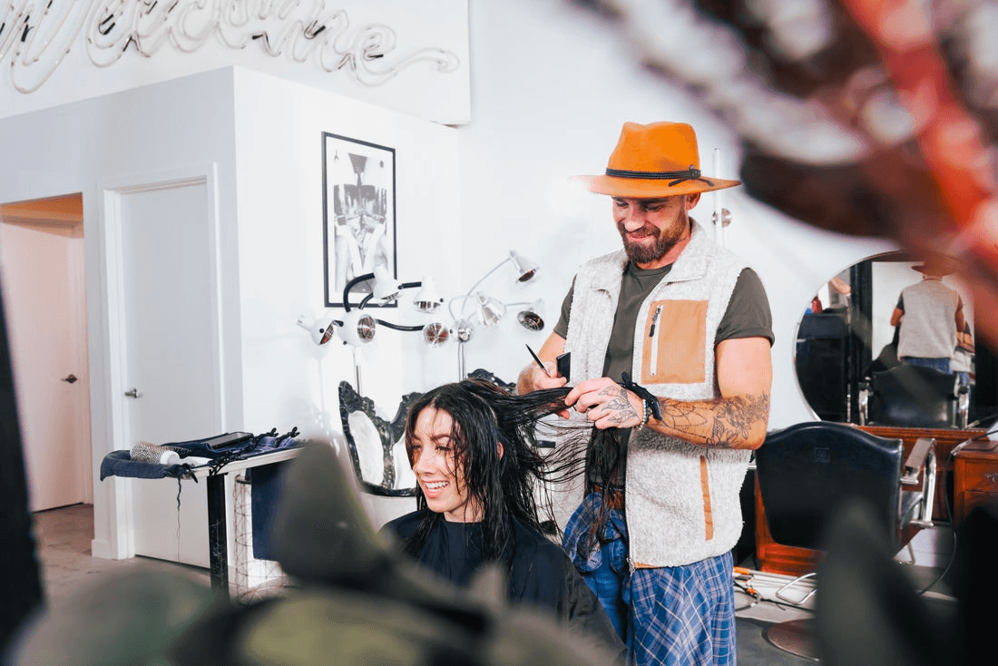 A man in an orange hat styles a woman's hair.